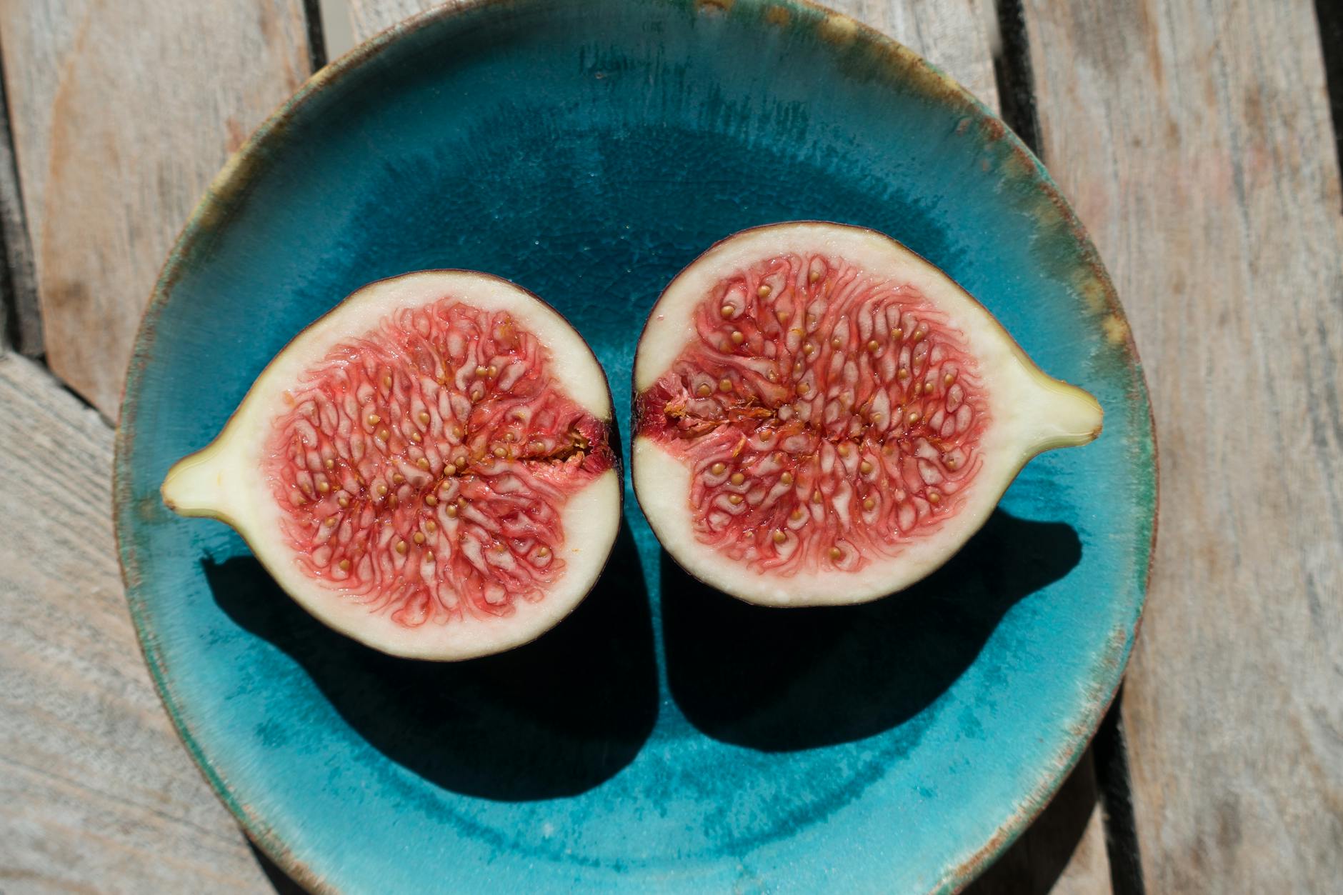 Close-up of a fresh ripe fig sliced in half on a vibrant blue plate outdoors.