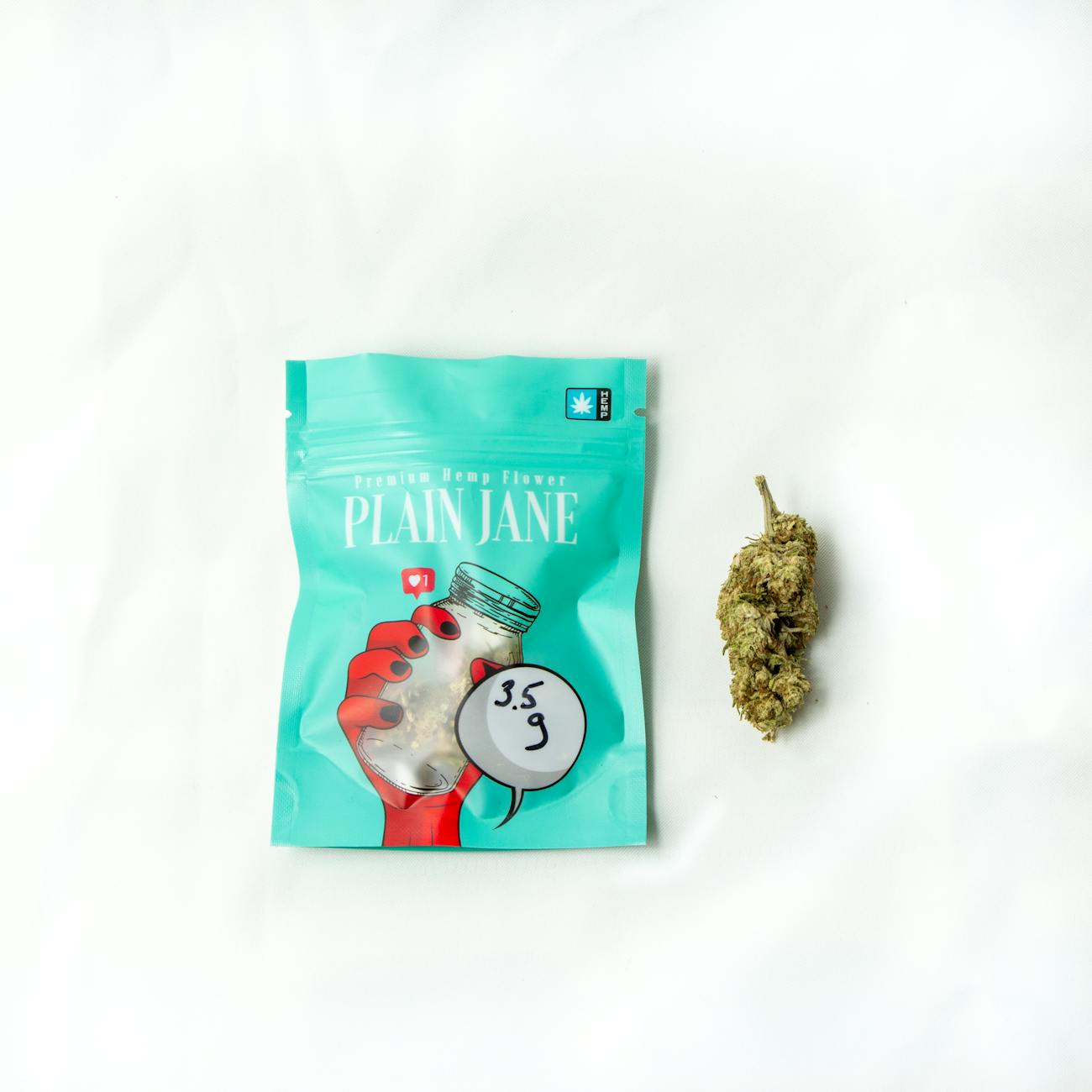 Close-up of premium cannabis bud and distinctive packaging on a seamless white surface.